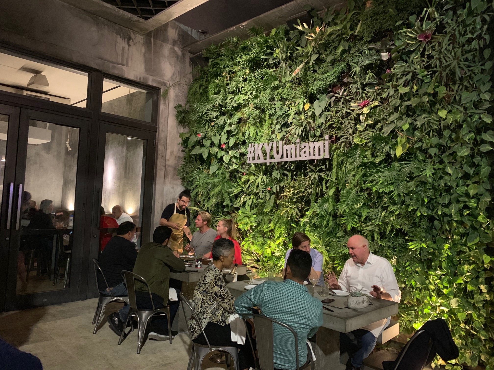 Restaurant guest at KYU in Miami, FL, dining in front of living green wall maintained by Miami Vertical Garden